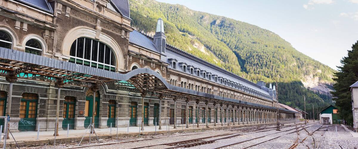 A historic train station with a large dome and arched windows, set against a mountainous backdrop.