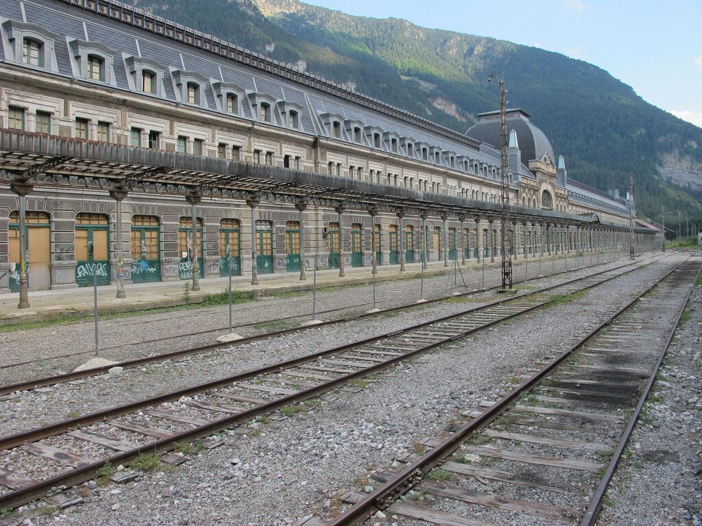A long, empty railway station with multiple tracks and a large building with a dome and arched windows.
