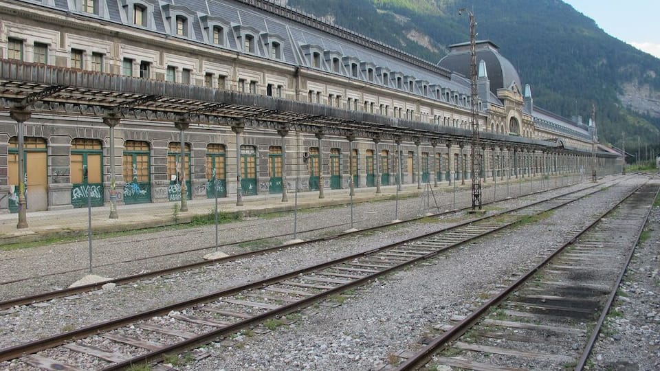 A long, empty railway station with multiple tracks and a large building with a dome and arched windows.