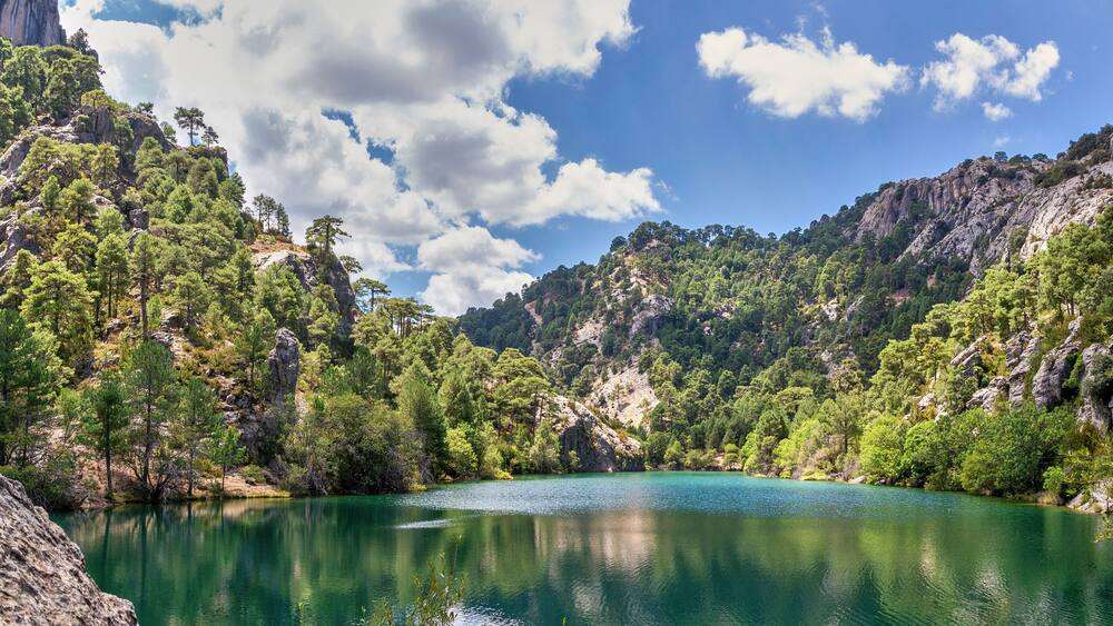 A turquoise lake surrounded by rocky cliffs and dense green forests.