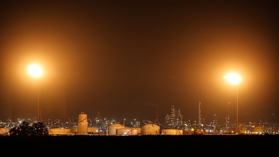 A nighttime industrial area with large storage tanks and bright streetlights.