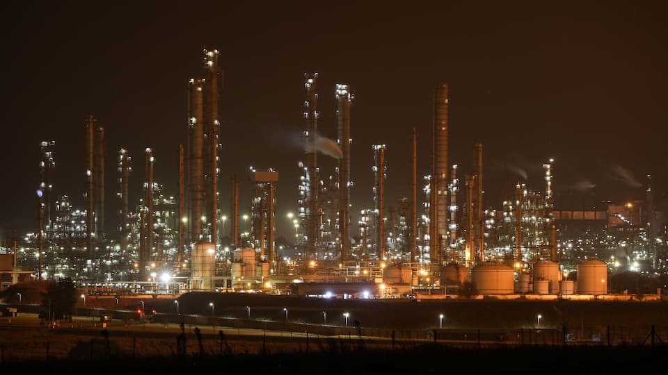 An industrial facility at night with illuminated structures and storage tanks.