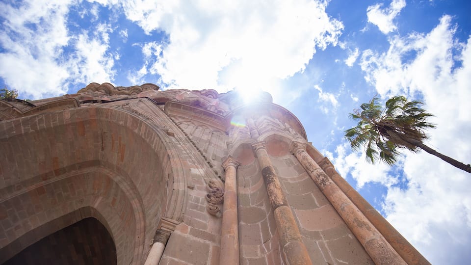 An ancient stone structure with large columns and an arched entrance under a clear sky.