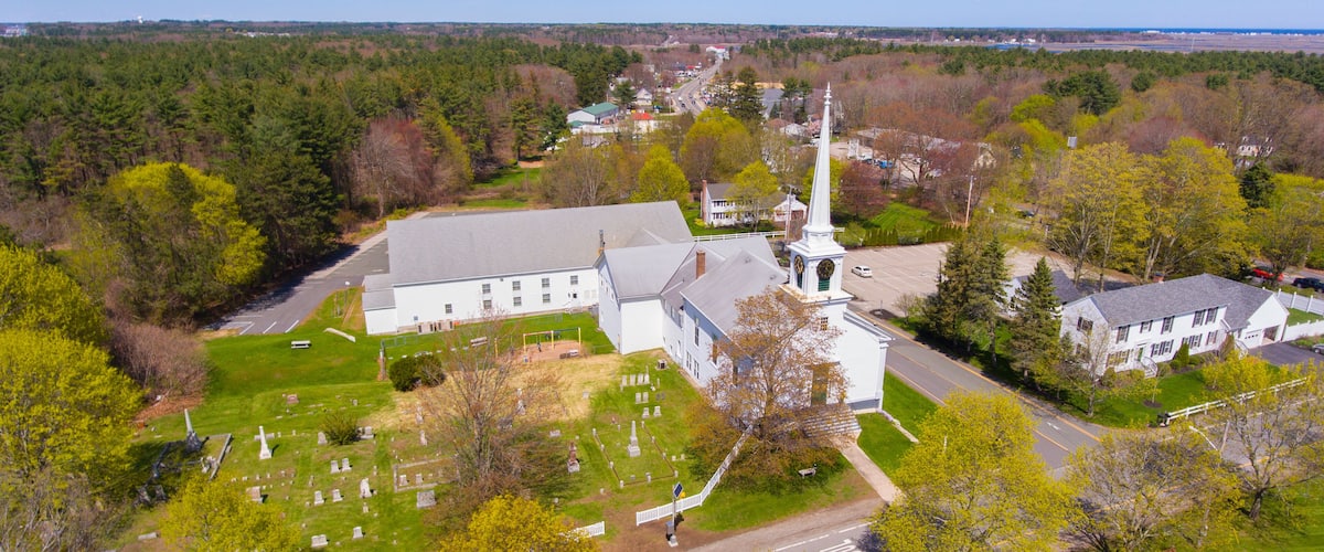 A church with a steeple, a cemetery, and surrounding greenery.