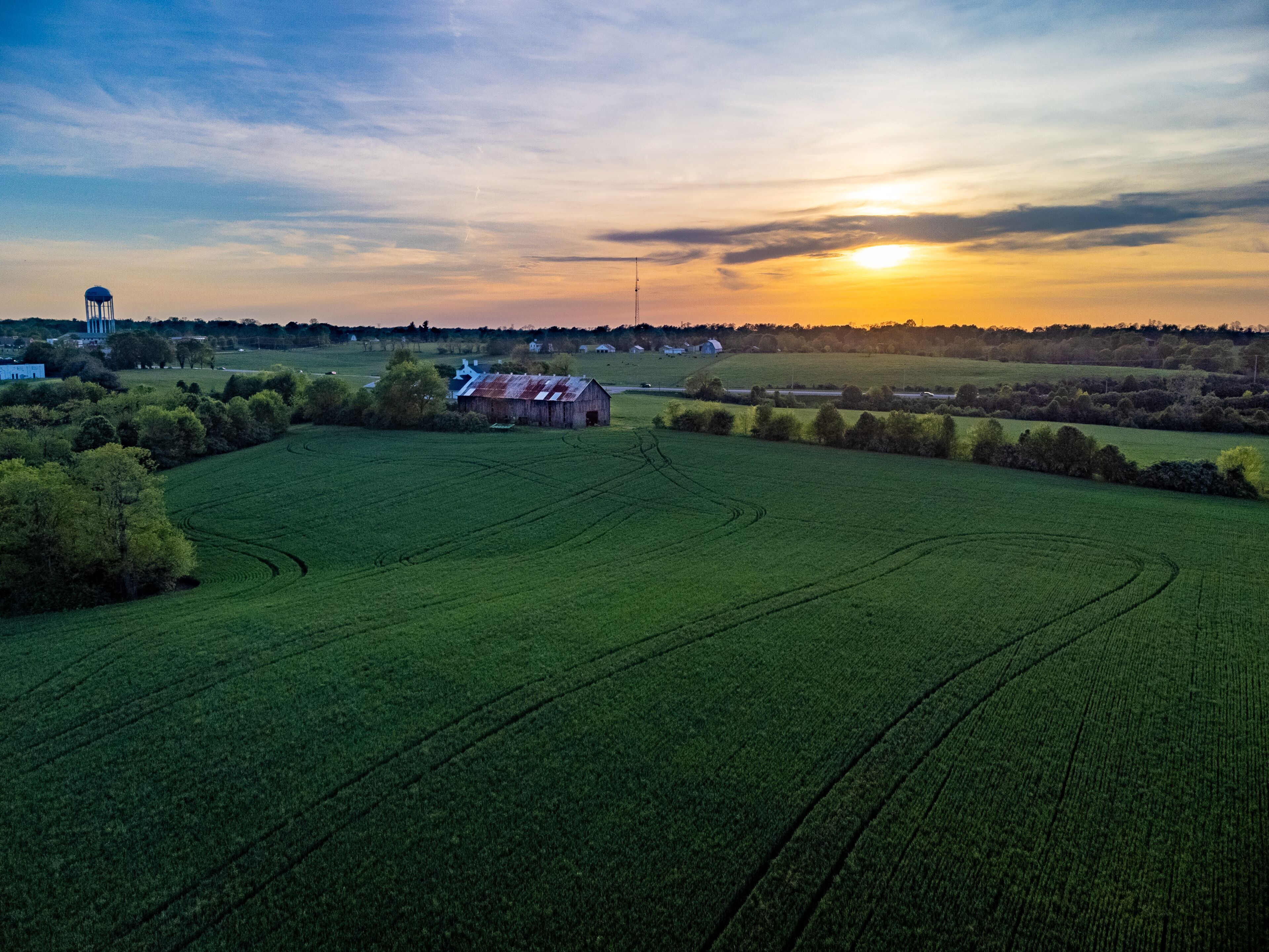 A rural landscape with a barn, water tower, and fields at sunset.