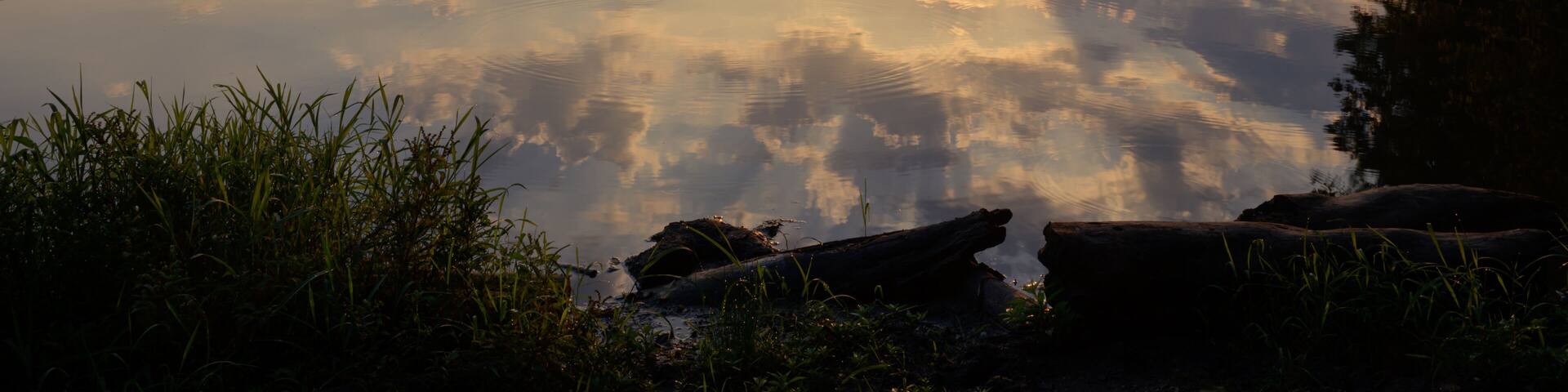 Sunrise over a calm small lake surrounded by a forest. Partly cloudy with sun rising over forested hills with a burst of sun rays and glowing clouds. Calm and peaceful
