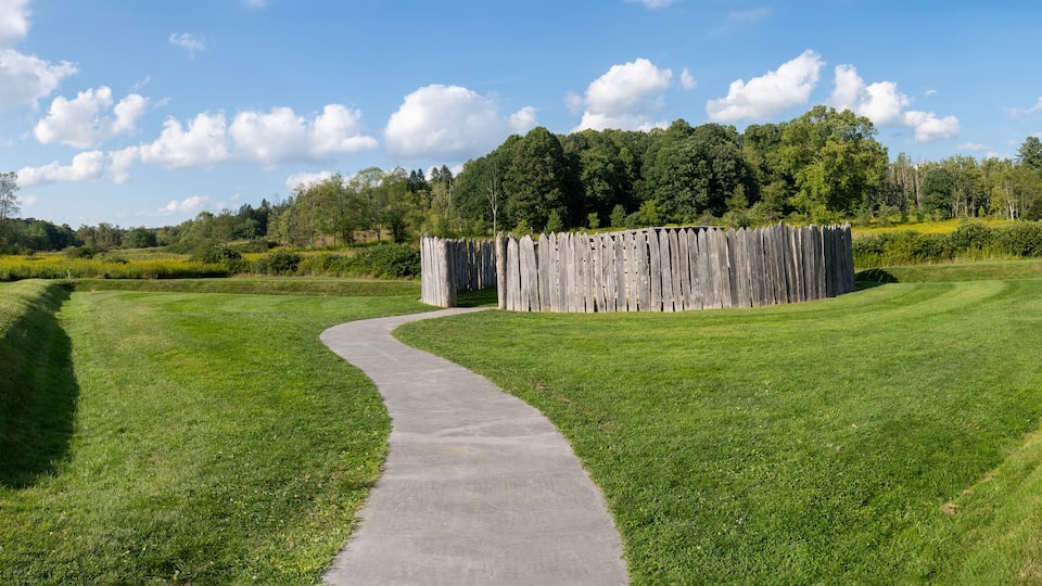 A winding concrete path through a well-maintained grassy area with a wooden fence and a telescope in the distance.