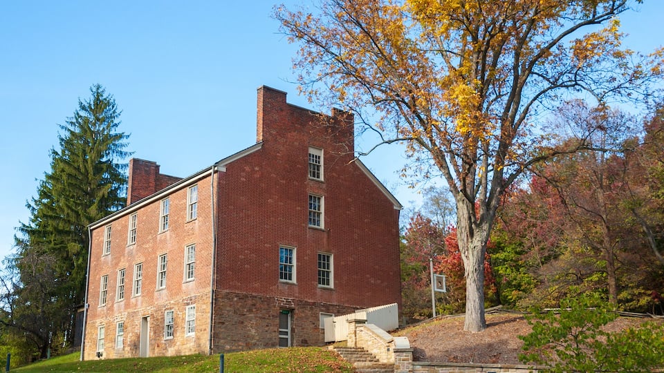 A red brick building with a stone foundation, surrounded by autumn foliage and a large tree.