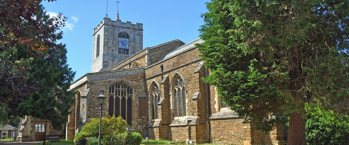 A historic church with a clock tower, surrounded by trees and a well-maintained garden.