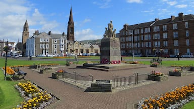 A town square with a statue, flower beds, and historic buildings.
