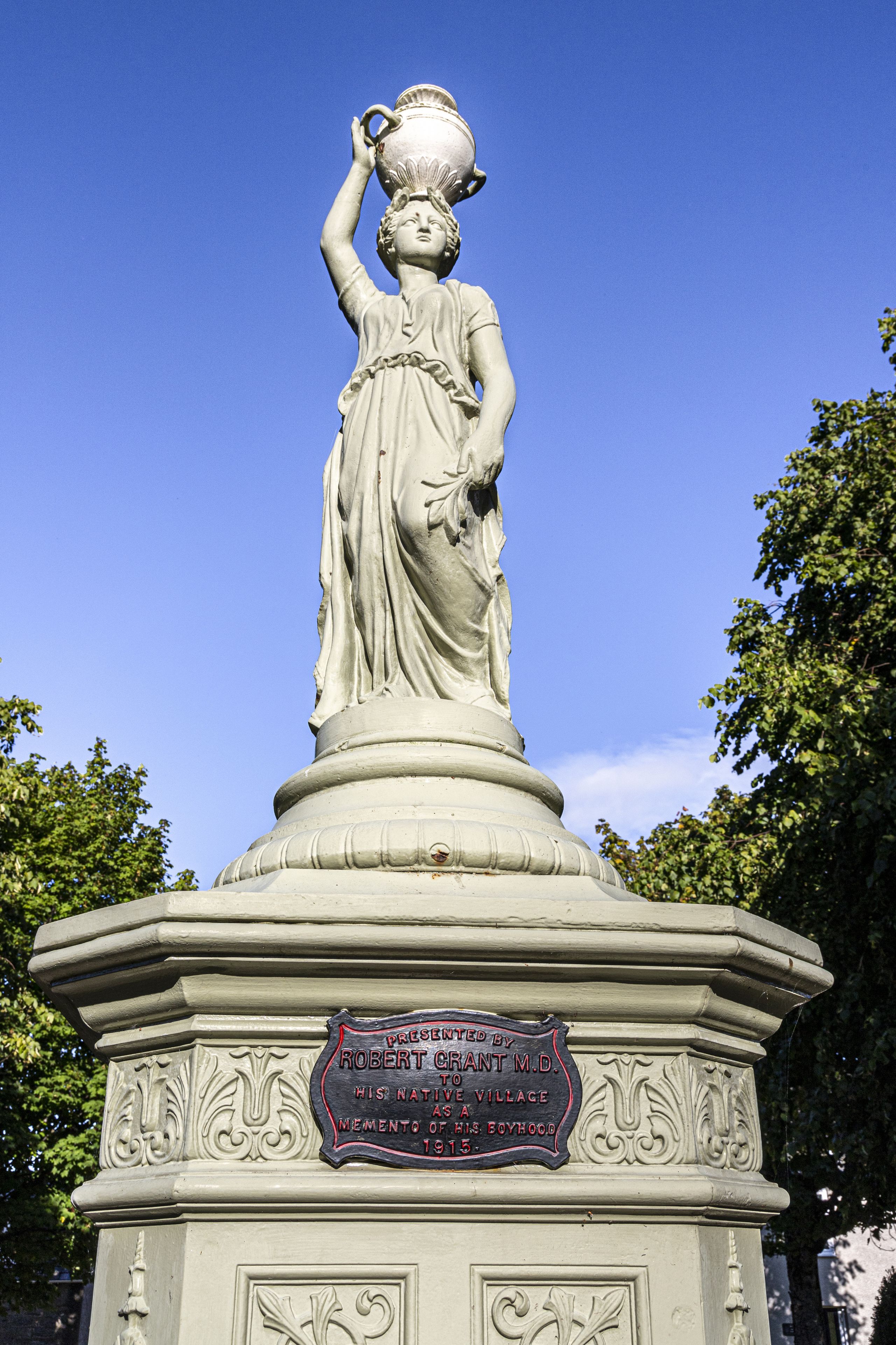 Une statue représentant une femme tenant un bol, placée sur un piédestal sur lequel est fixée une plaque commémorative.