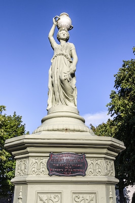 A statue of a woman holding a bowl, standing on a pedestal with a commemorative plaque.