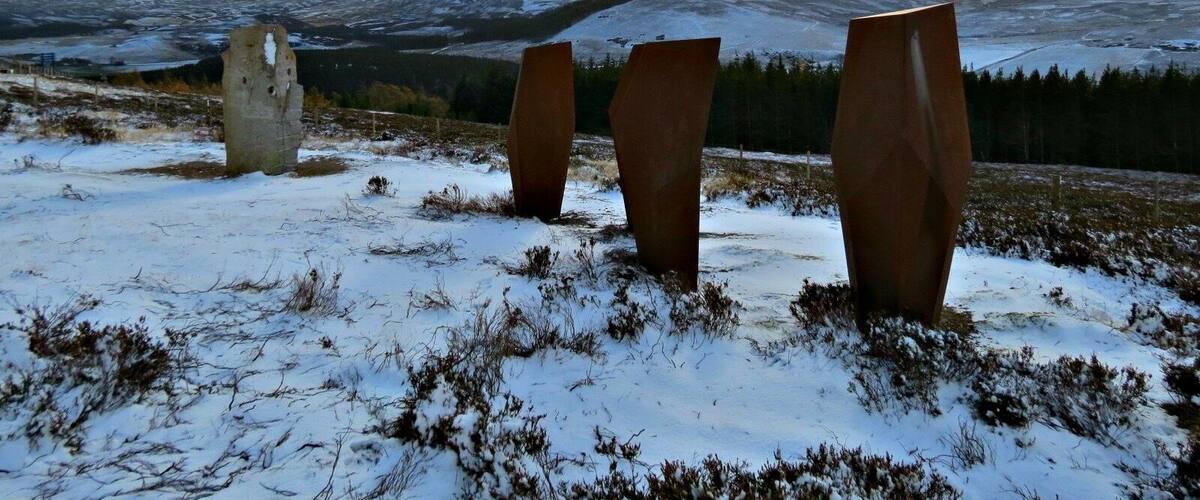 A snowy landscape with three metal sculptures and a stone structure.