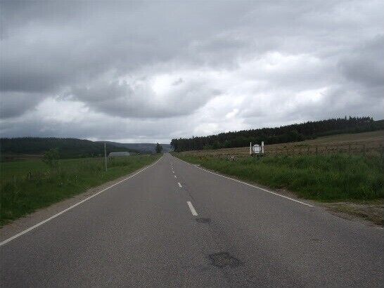 A rural road with grassy fields and a cloudy sky.