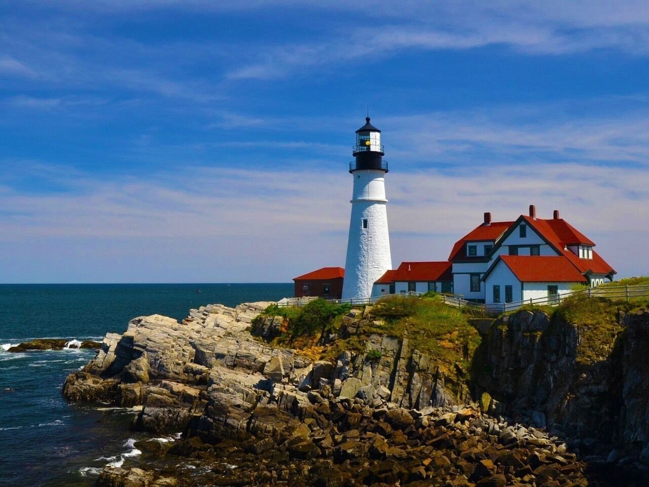 A lighthouse and a house with a red roof by the sea.