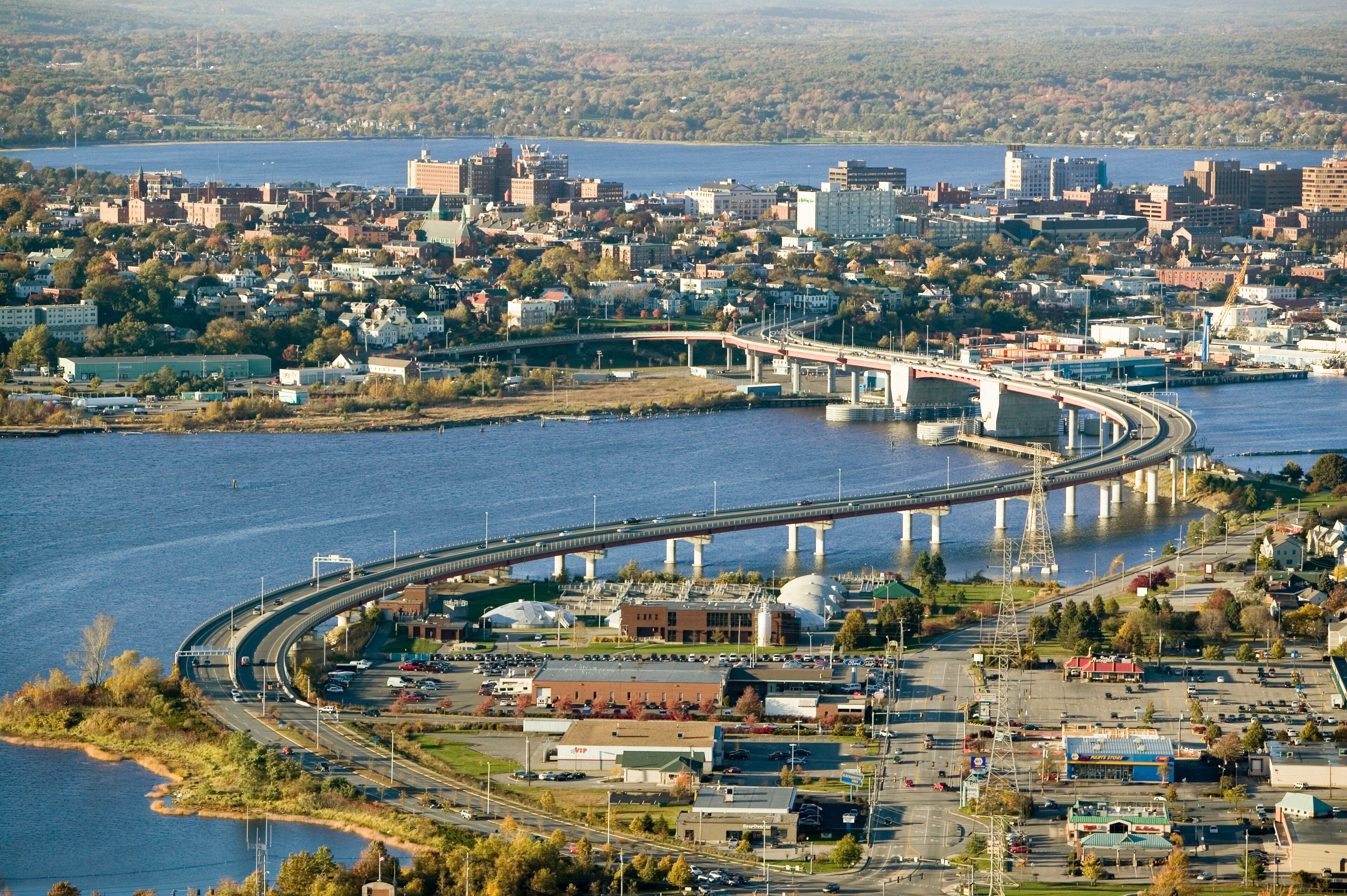 A river with a bridge, a parking lot, and buildings in the background.