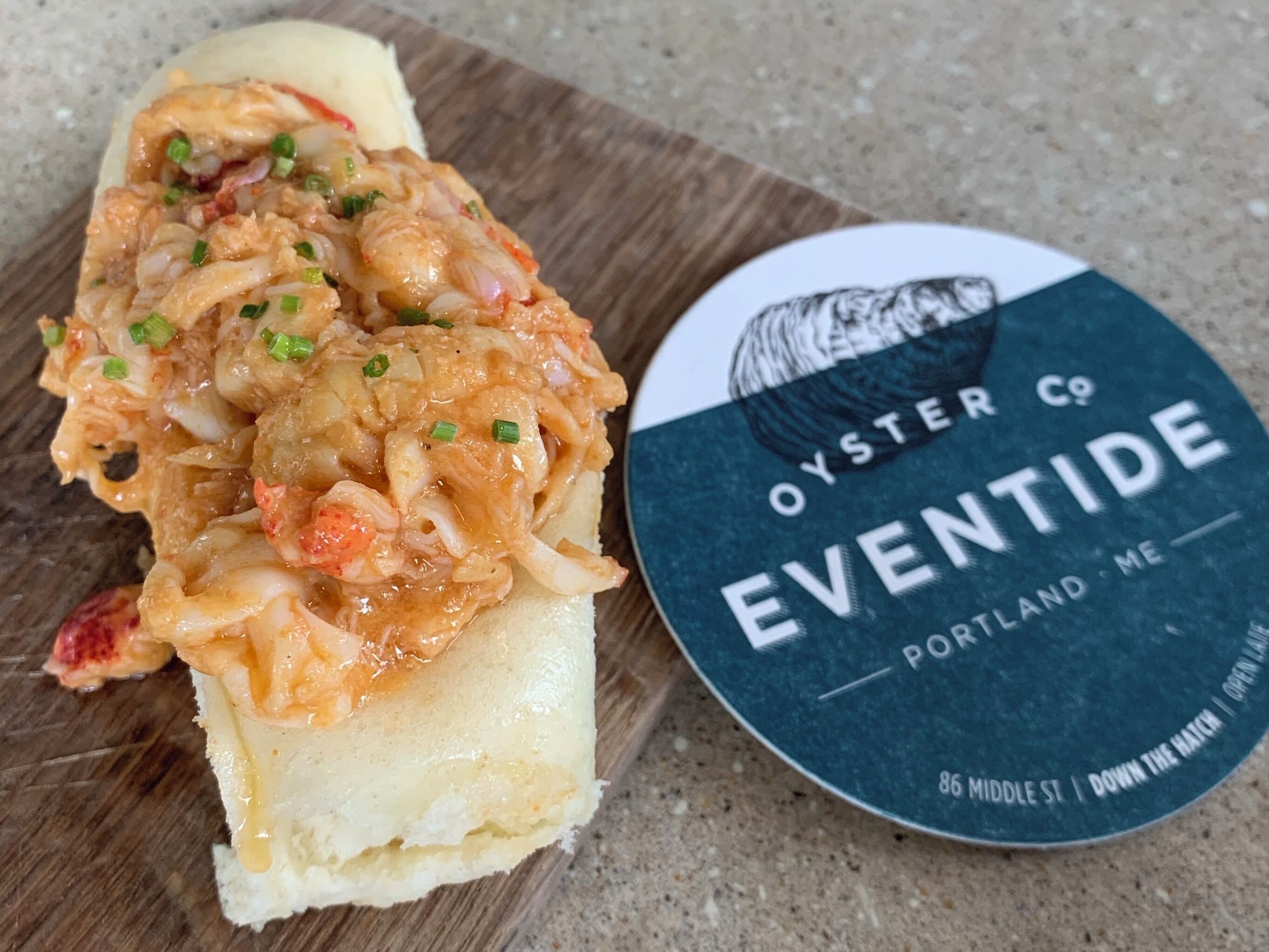 A sandwich with a topping of shrimp and onions, and a container labeled 'Oyster Co Eventide Portland ME'.