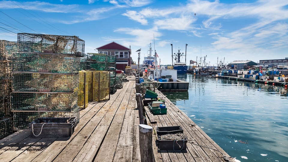 A wooden pier with fishing cages and boats docked in a harbor.
