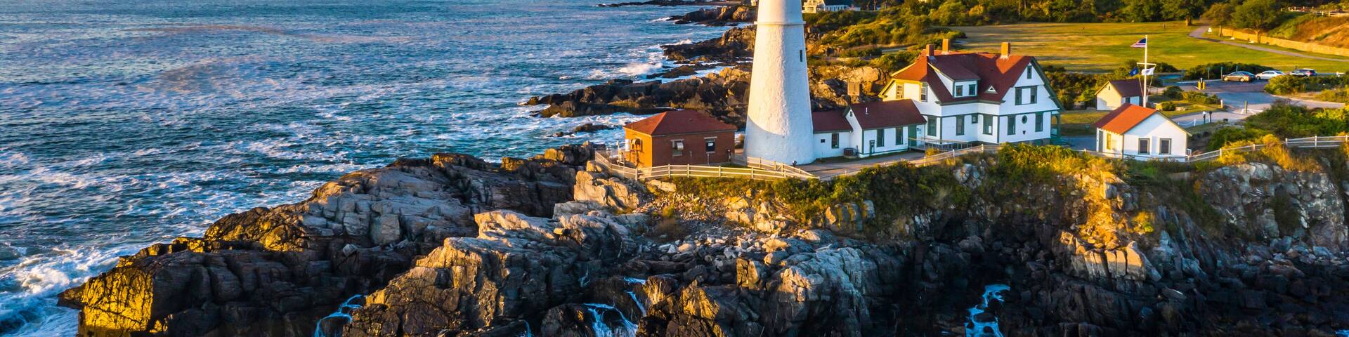 A lighthouse and houses on a rocky coastline with the ocean in the background.