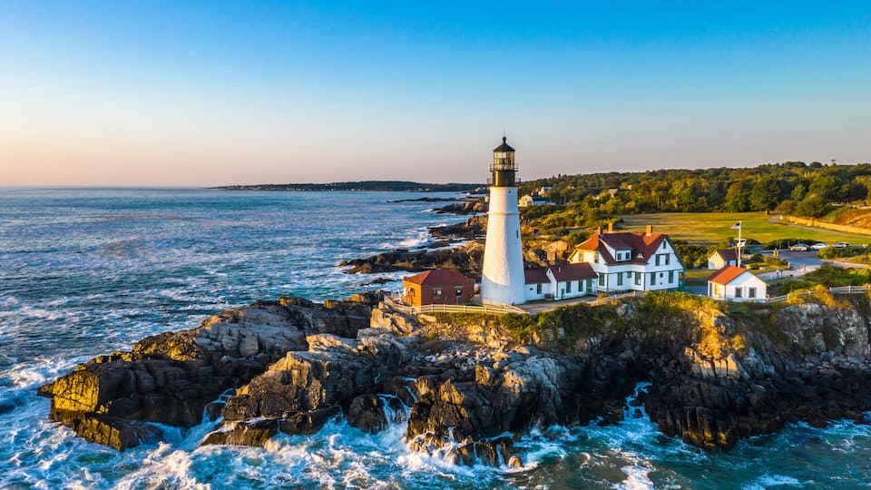 A lighthouse and houses on a rocky coastline with the ocean in the background.