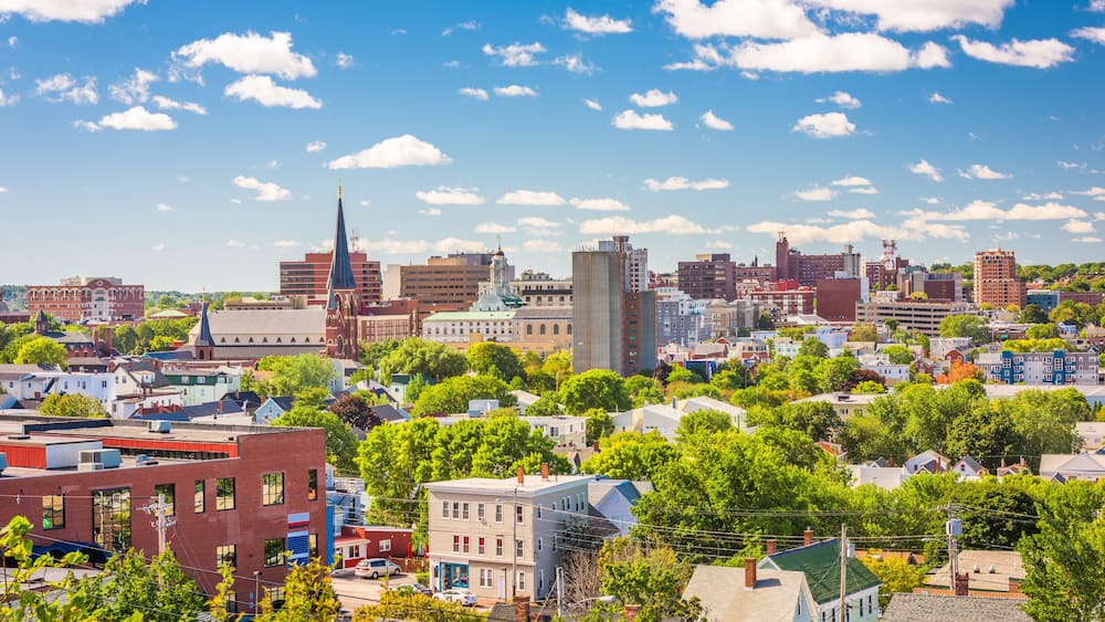A cityscape with a prominent church steeple, various buildings, and lush green trees.
