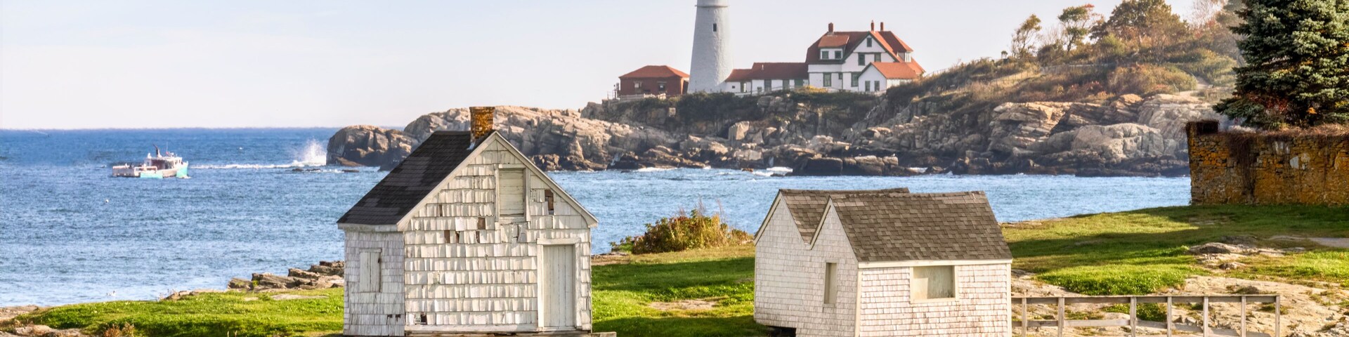 Old Fishing shacks per on a rocky shore of Fisherman’s Point with the Portland Head Light, a lighthouse along the Atlantic coast of Down East Maine in America’s New England region.