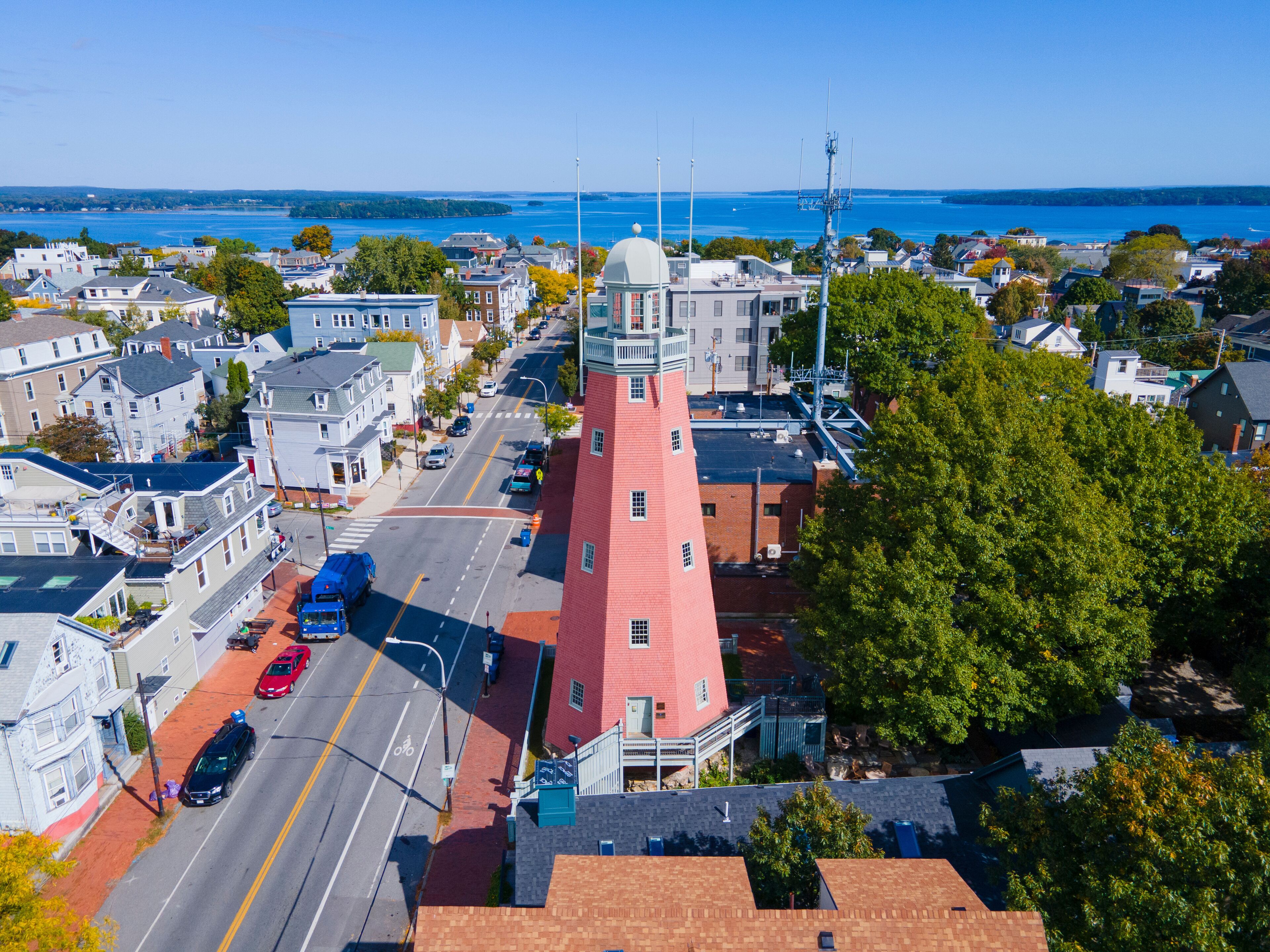 A coastal town with a prominent red tower, a clear blue sky, and a view of the sea.