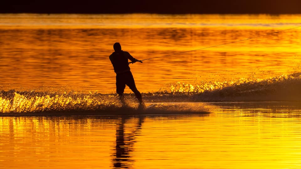 A person wakeboarding on a body of water during sunset.