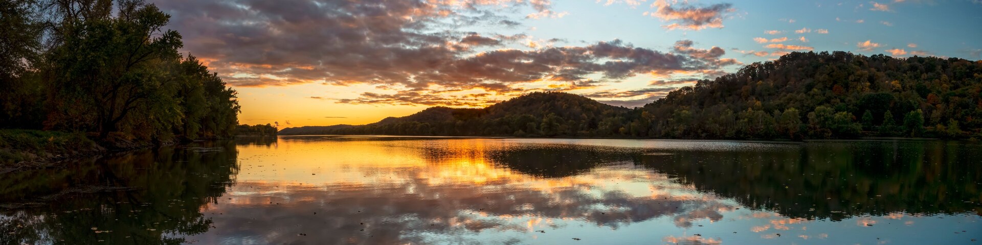 Un lago tranquilo reflejando el cielo al atardecer con árboles en la orilla.
