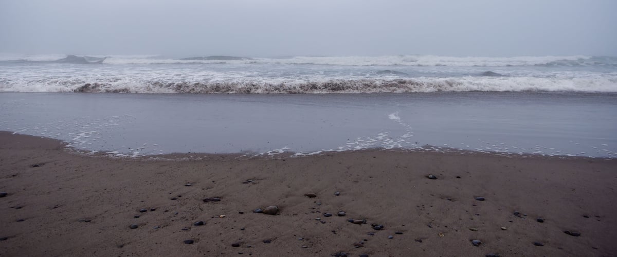 A beach with waves crashing onto the shore and scattered rocks.