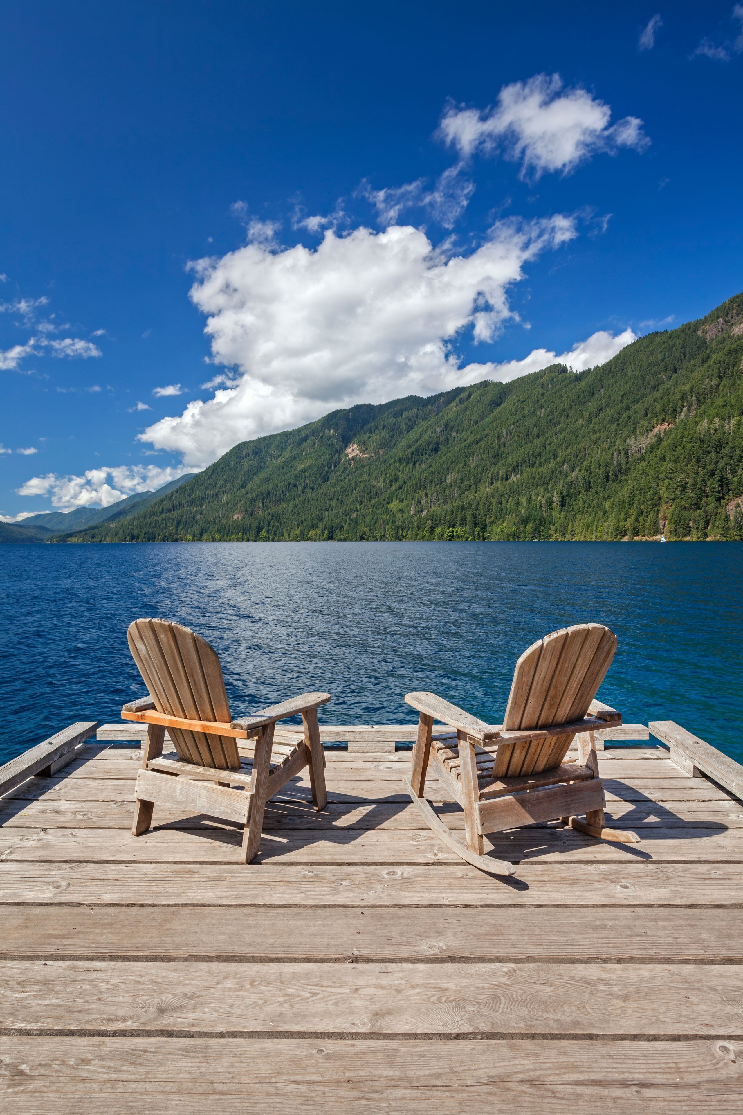 Two Adirondack chairs rest on a wooden dock with views of Lake Crescent and surrounding mountains in Olympic National Park, Washington.