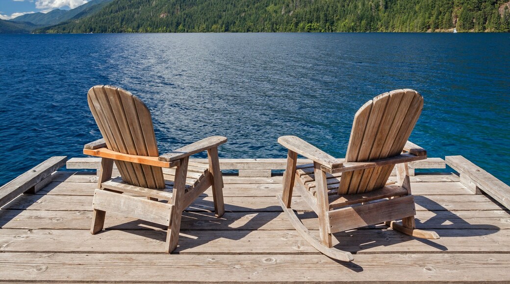 Two Adirondack chairs rest on a wooden dock with views of Lake Crescent and surrounding mountains in Olympic National Park, Washington.