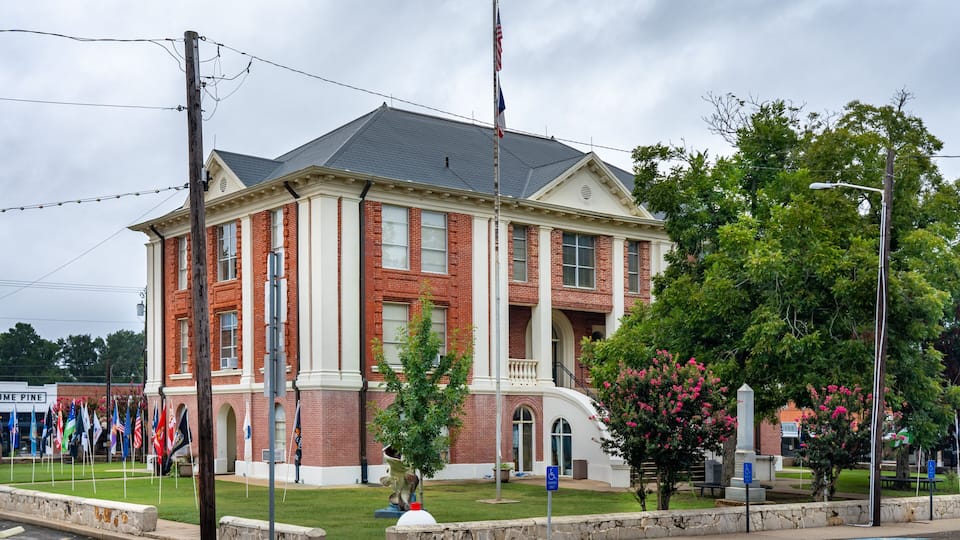 A red-brick courthouse with a flagpole, a lawn, and a street lamp.