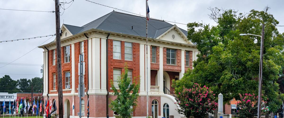 A red-brick courthouse with a flagpole, a lawn, and a street lamp.
