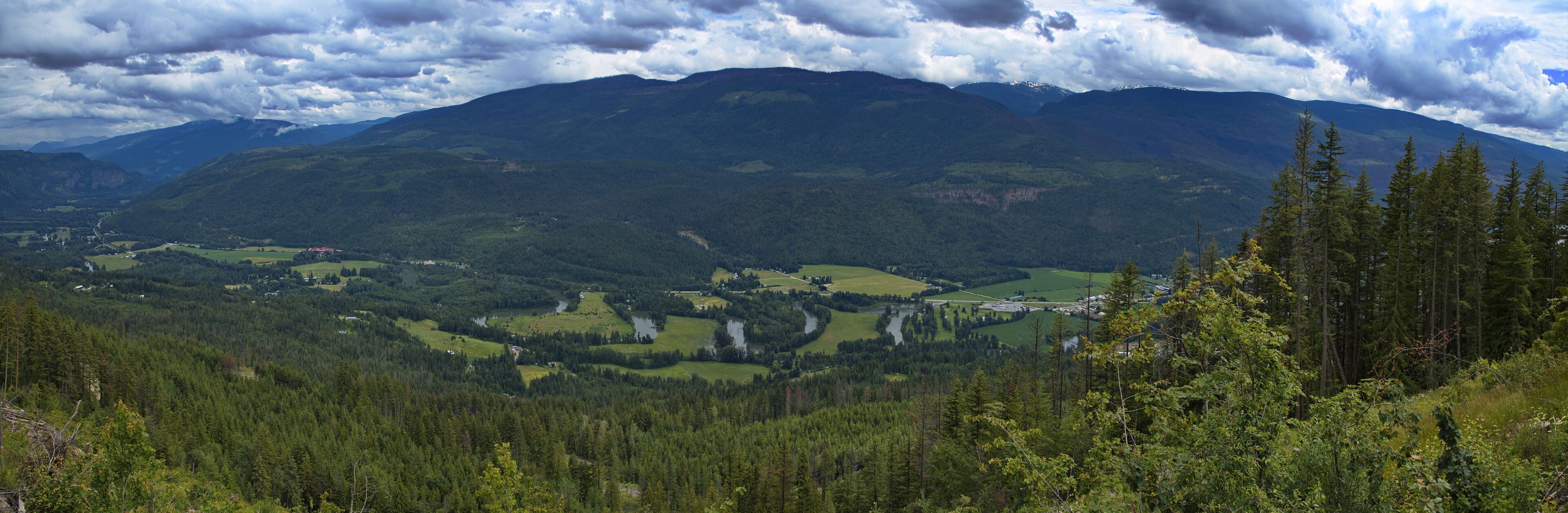 A mountainous landscape with dense forests, a river, and scattered buildings.