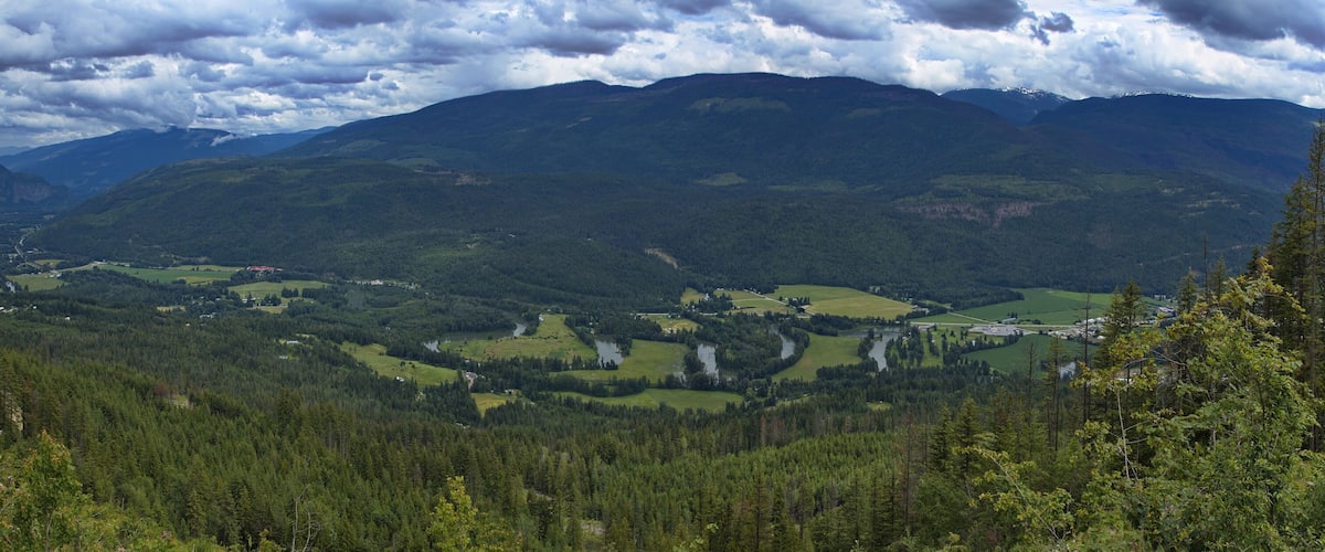 A mountainous landscape with dense forests, a river, and scattered buildings.