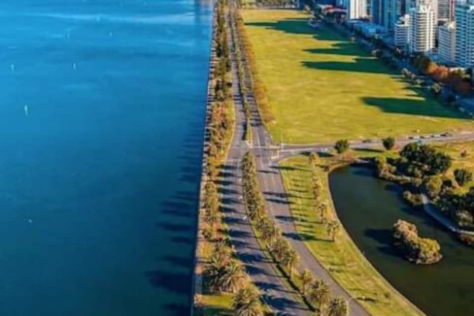A coastal cityscape with a long promenade along the waterfront, a park, and modern high-rise buildings.