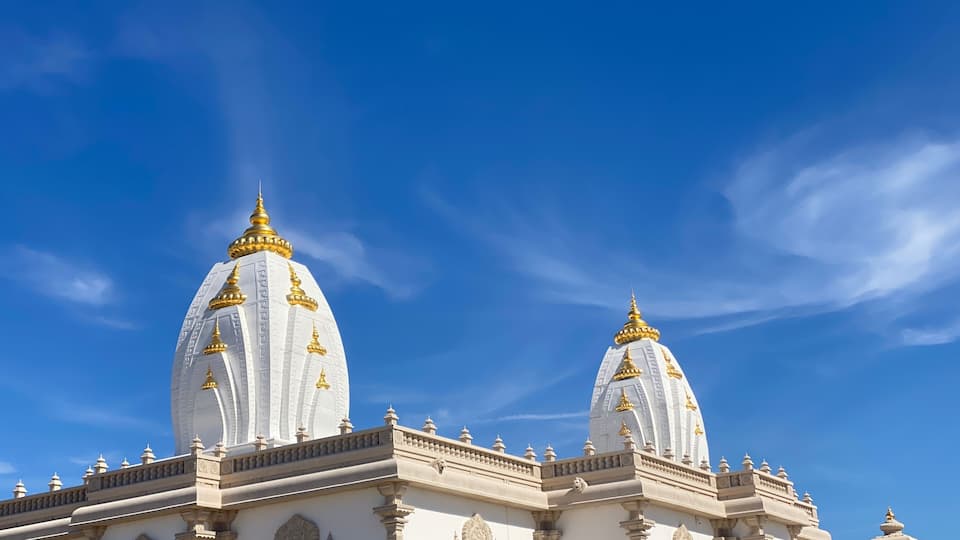 A white building with golden domes and intricate carvings under a clear blue sky.
