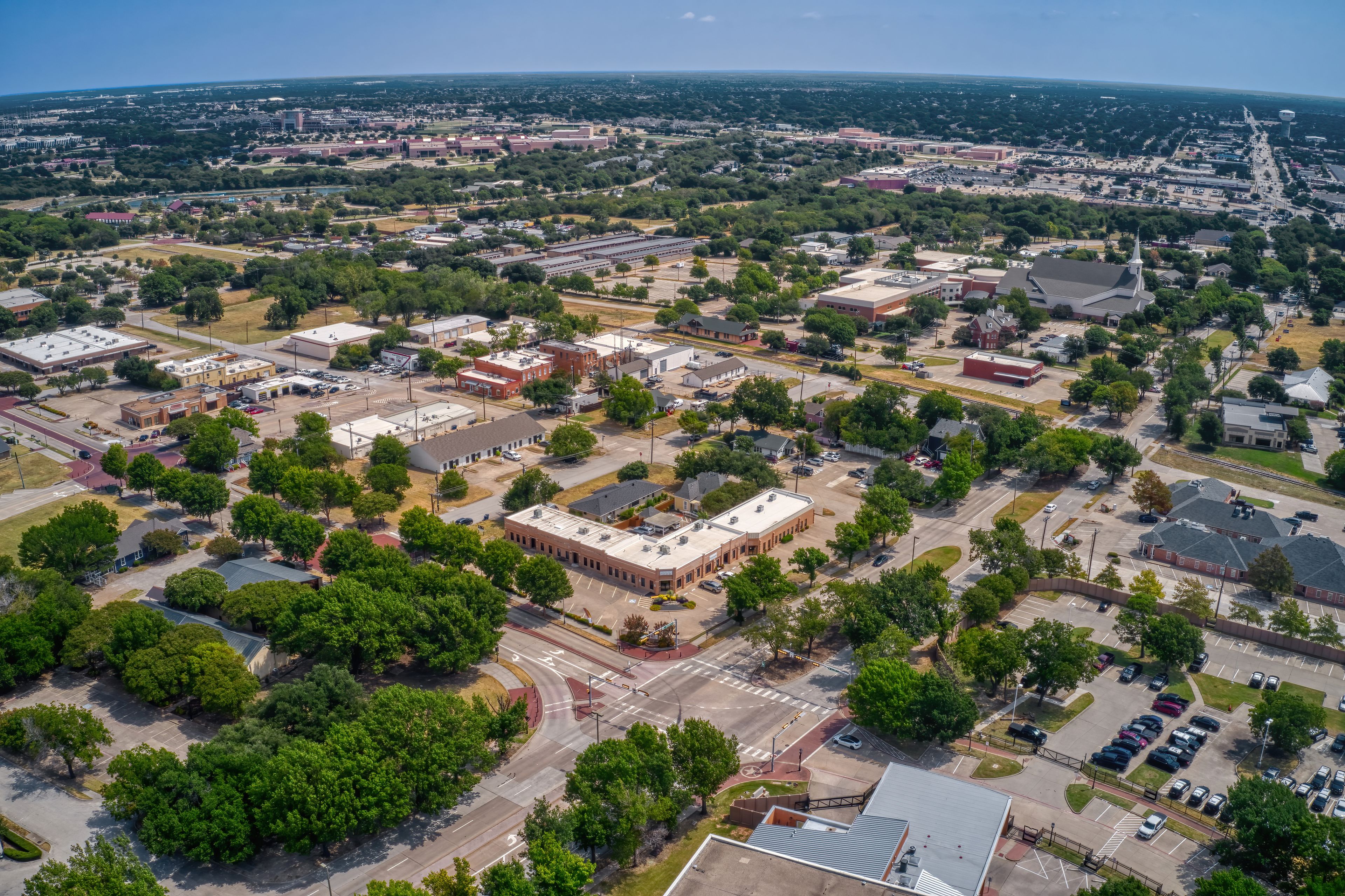 An aerial view of a city with a mix of commercial buildings, roads, and green spaces.