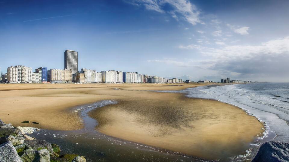 A coastal cityscape with a sandy beach, a large body of water, and a row of high-rise buildings.