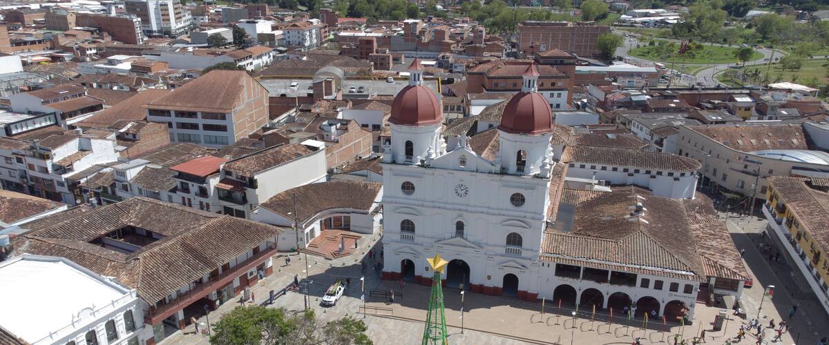 An aerial view of a historic town with a prominent white church with two domes, surrounded by traditional buildings with red-tiled roofs.