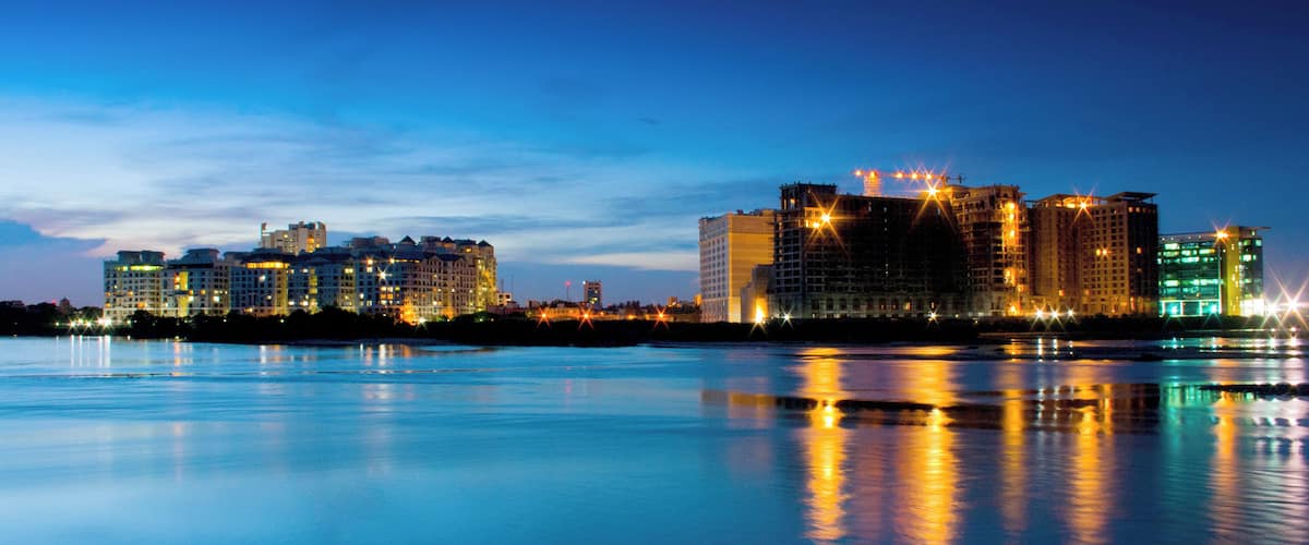 A nighttime cityscape with illuminated buildings reflecting on calm water.