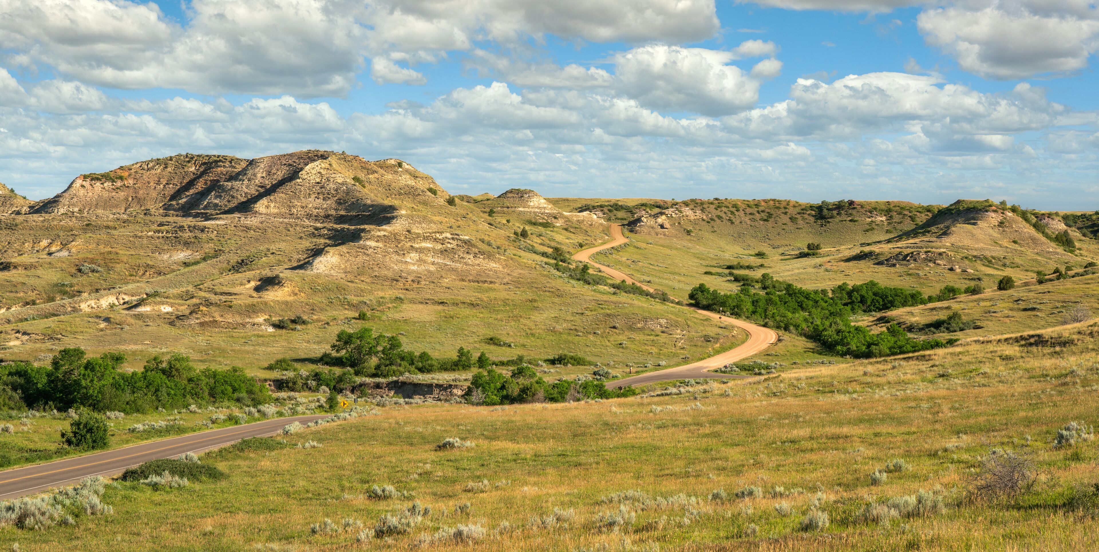 A winding road through a hilly landscape with sparse vegetation and a clear sky.