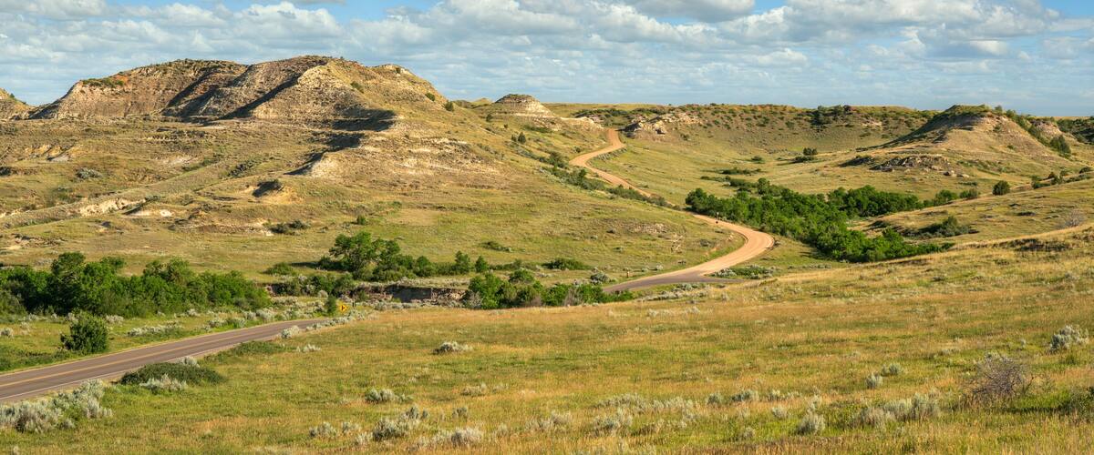 A winding road through a hilly landscape with sparse vegetation and a clear sky.
