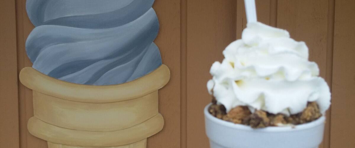 A hand holding a cup of ice cream with a white cone and a spoon.