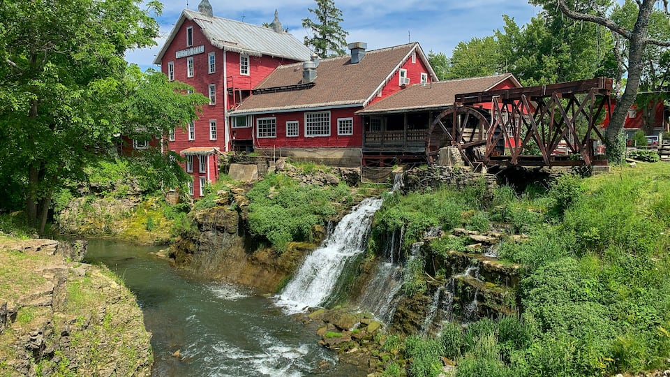 A red mill with a water wheel and a waterfall.