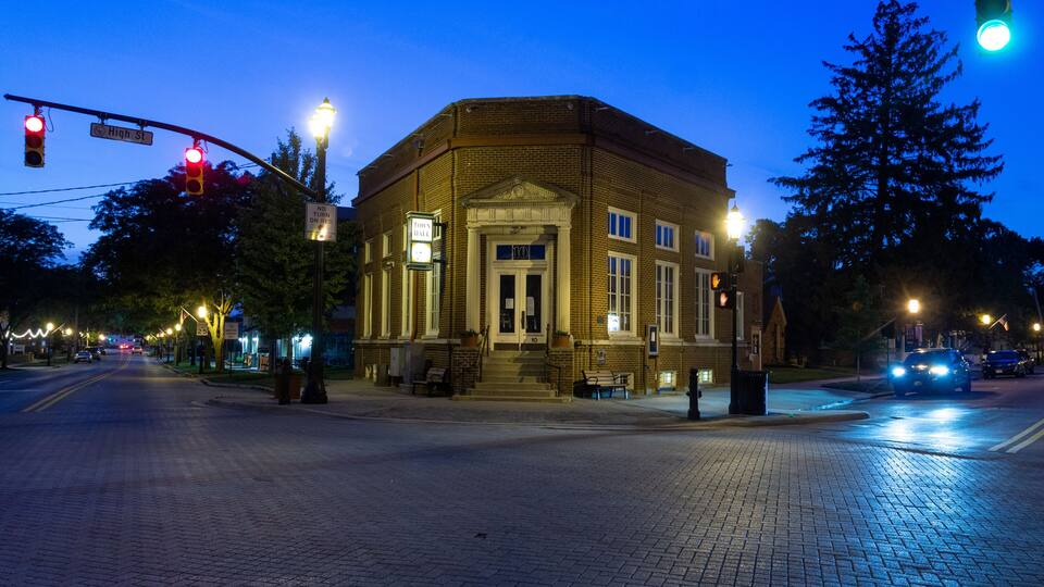 A brick building with a pedimented entrance, street lamps, and traffic lights at a crosswalk.
