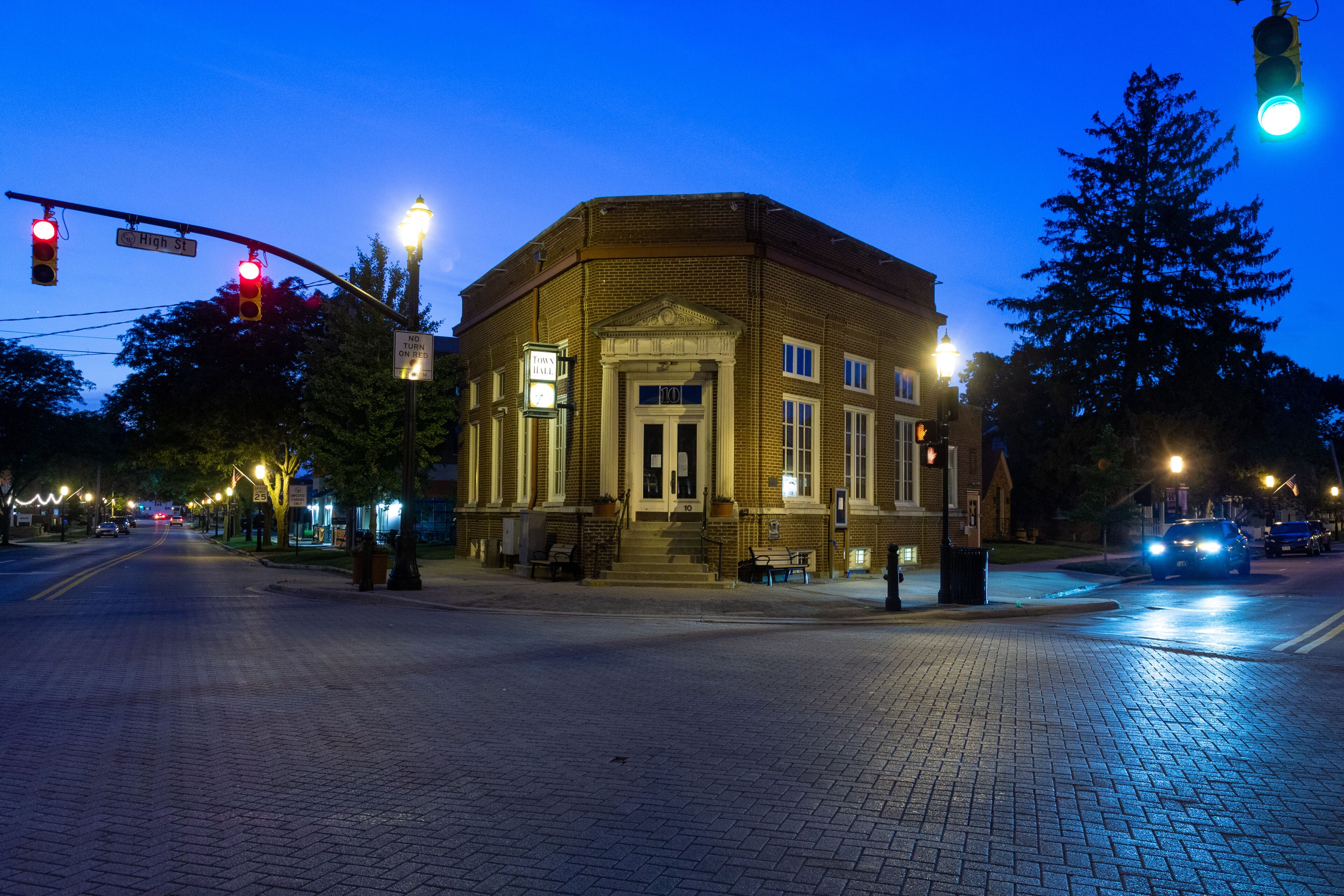 A brick building with a pedimented entrance, street lamps, and traffic lights at a crosswalk.