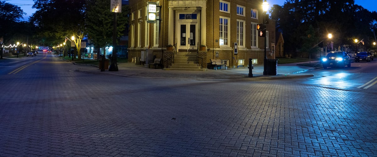 A brick building with a pedimented entrance, street lamps, and traffic lights at a crosswalk.