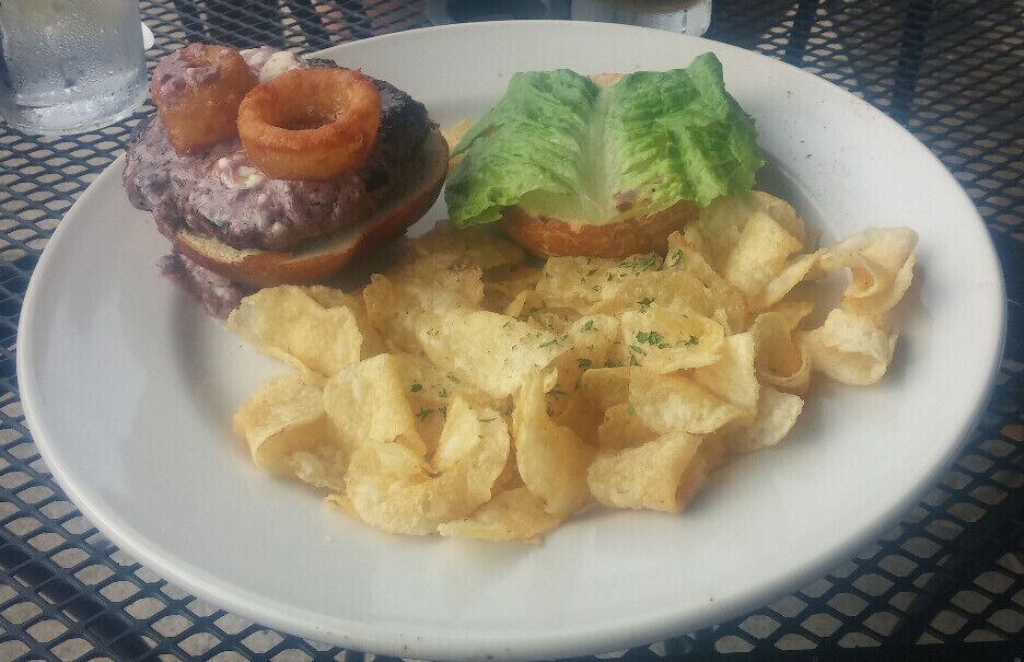 The Butter Bison Burger topped with house-made compound butter (Maytag bleu cheese, butter, bone marrow, red wine reduction), lettuce, onion rings, served on a pretzel roll.
